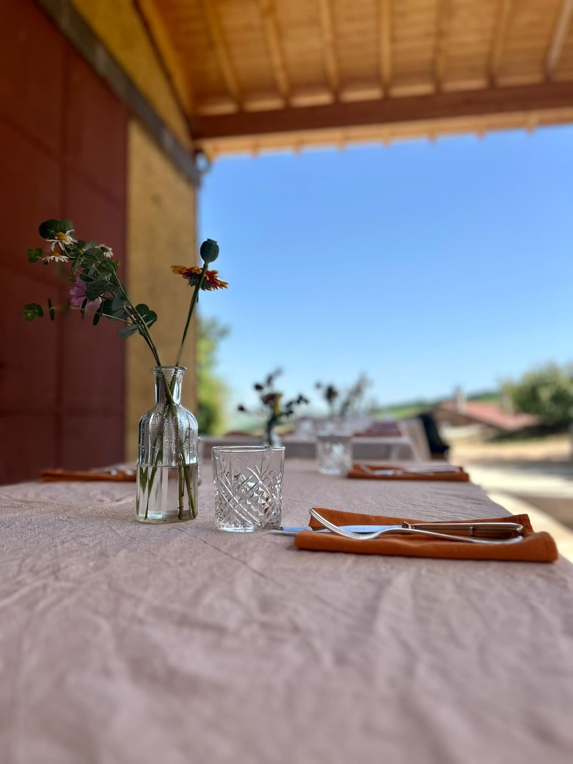Table dressée en terrasse face aux vignes, fleurs des champs et verres en cristal