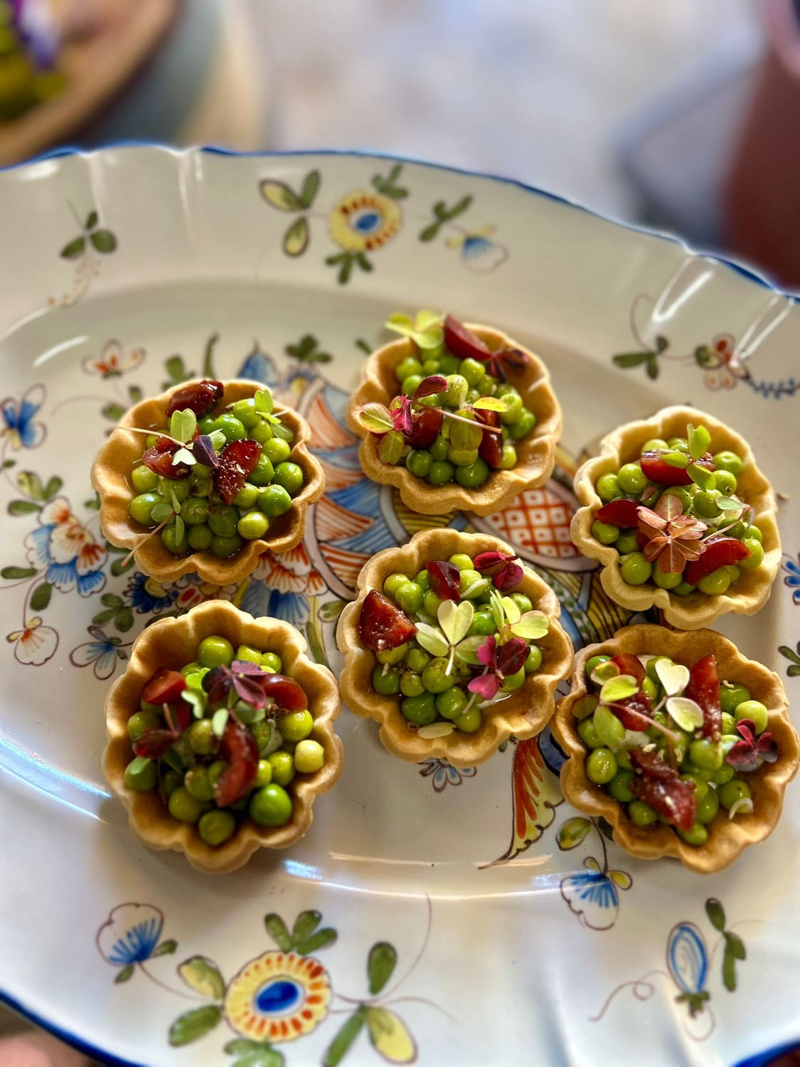 Tartelettes aux petits pois, cerises et jeunes pousses sur plat ancien fleuri